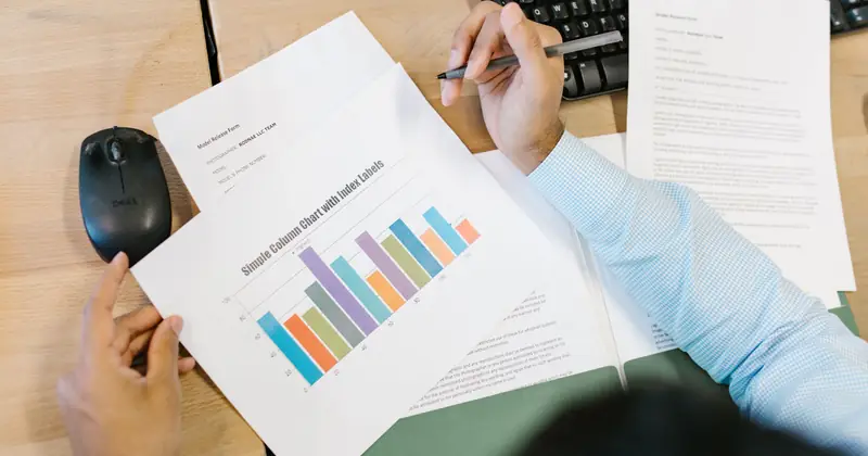 A business analyst reviews a colorful bar chart and documents at a desk, indicating data analysis.