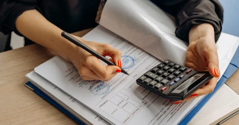 Hands checking figures beside a calculator