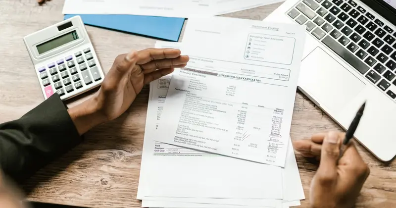An accountant reviewing a statement of account with a calculator and laptop to hand.