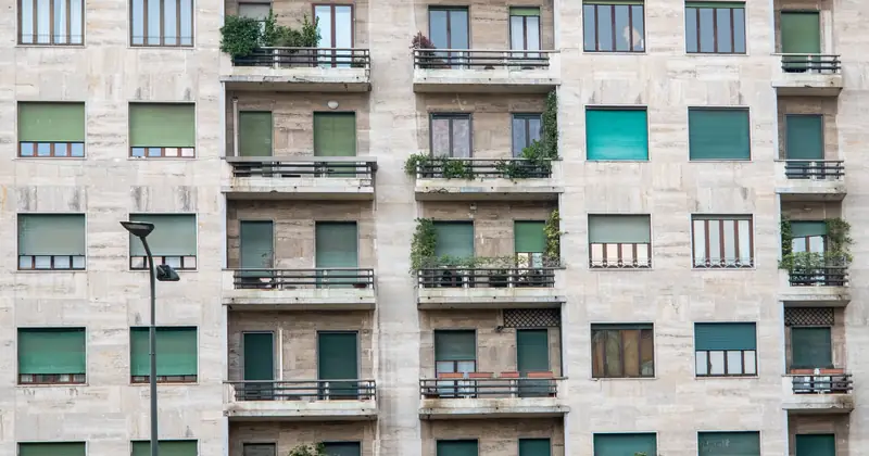Facade of a modern residential building in Milan with balconies and green shutters.