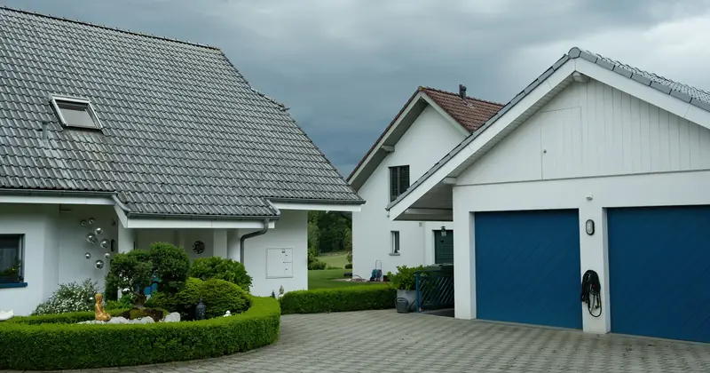 Lovely suburban houses with blue garage doors under cloudy sky, surrounded by greenery.