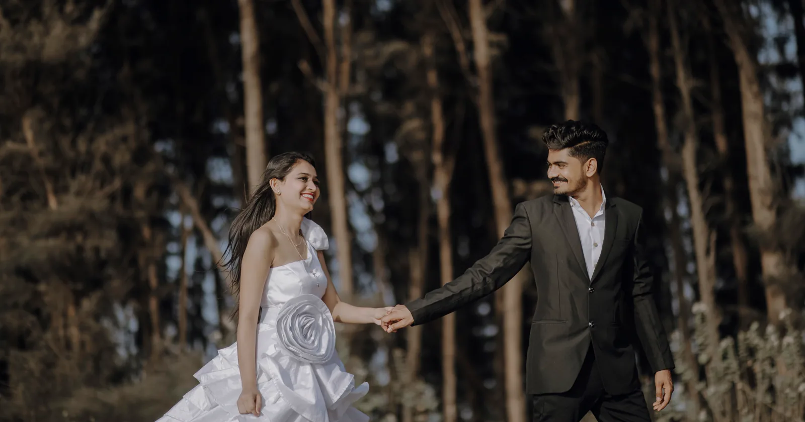 A couple holding hands beneath trees.