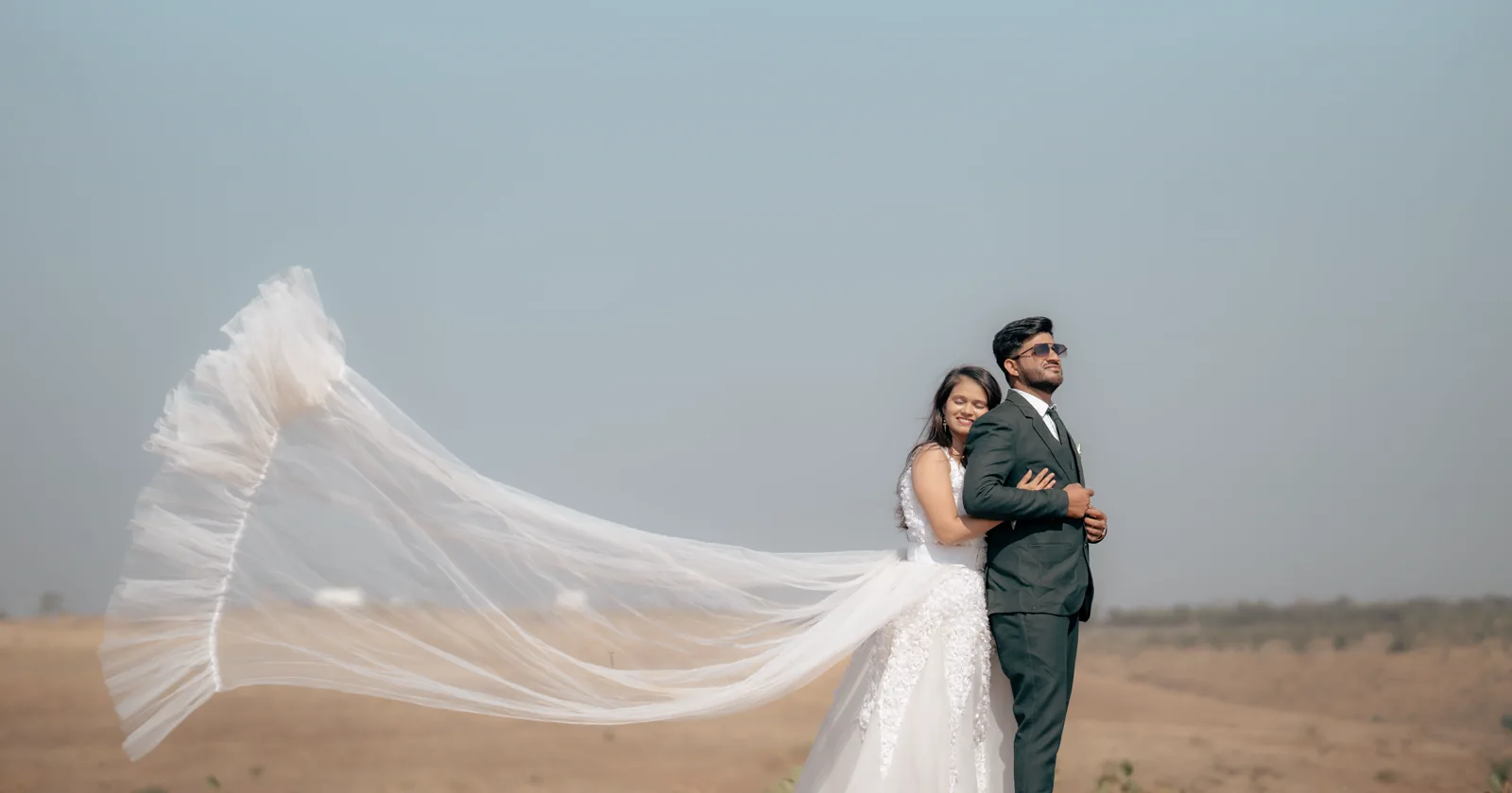 A couple walking outdoors with a veil moving in the breeze.