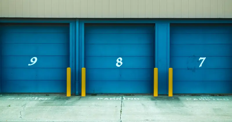 Three blue shutter doors numbered 9, 8, and 7 with yellow barriers in urban environment.