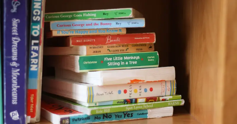 A stack of colourful storybooks on a wooden shelf.
