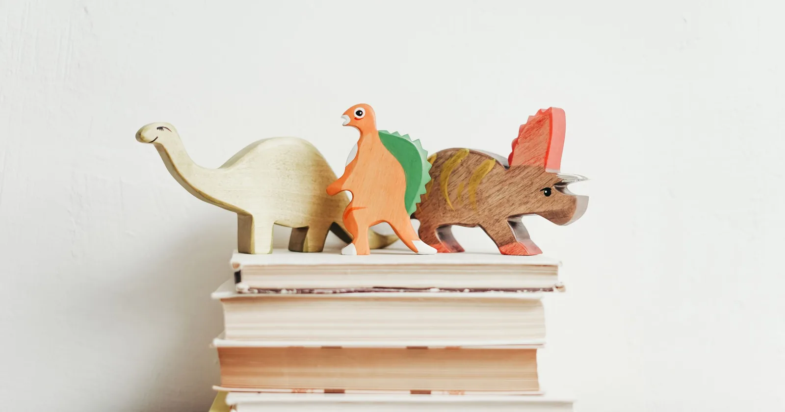 Wooden dinosaur figures on a stack of storybooks.