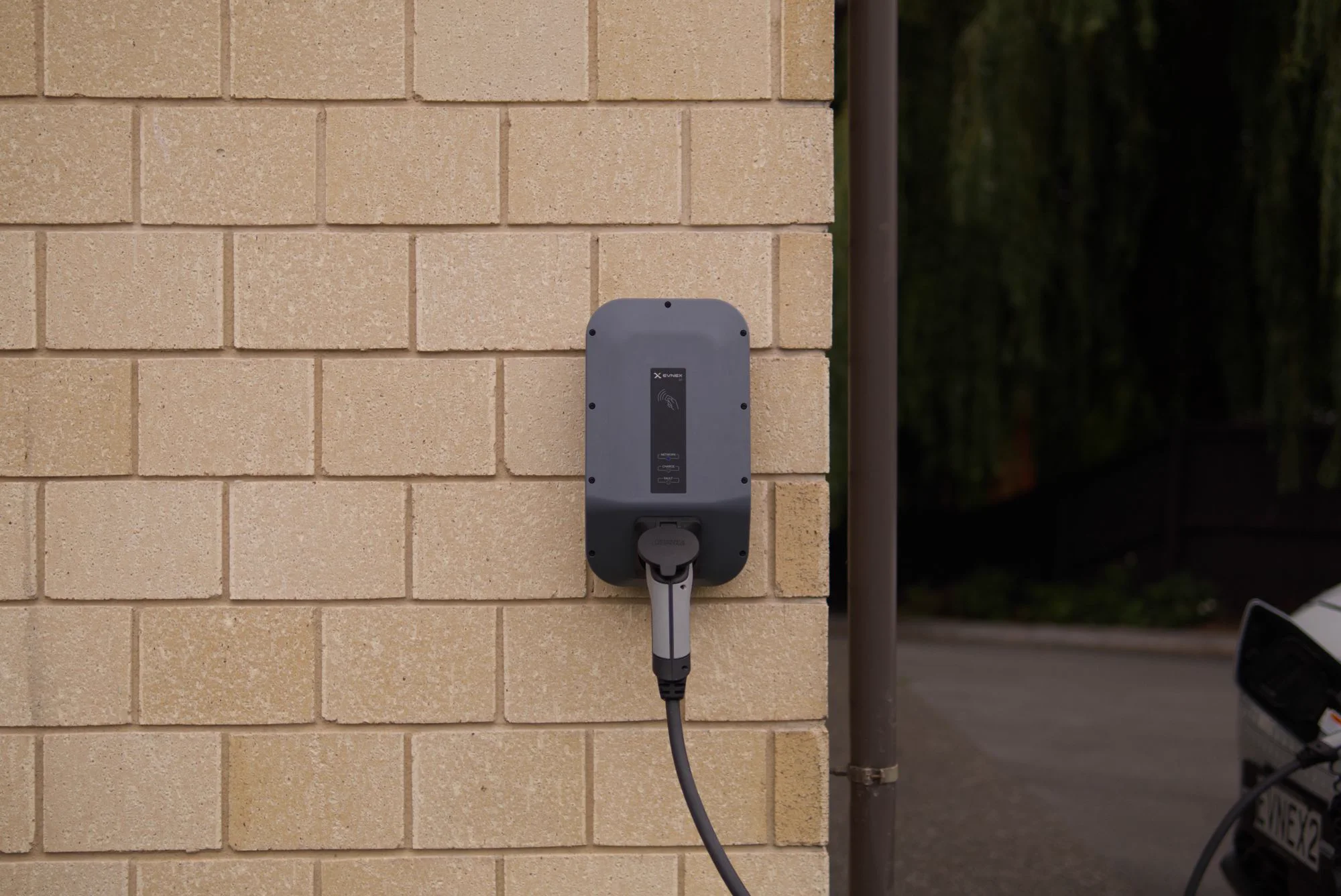 A wall-mounted electric vehicle charger beside a domestic driveway.